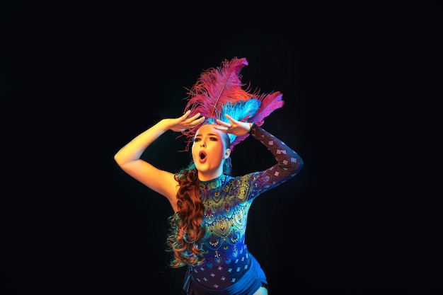 Photo gratuite belle jeune femme en carnaval, costume de mascarade élégant avec des plumes sur un mur noir en néon