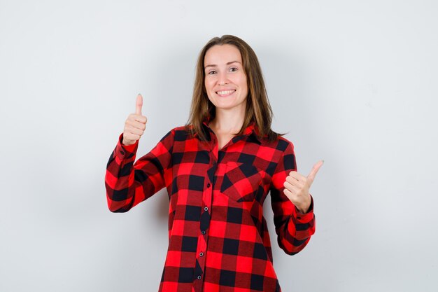 Belle jeune femme en chemise décontractée montrant les pouces vers le haut et à la béatitude, vue de face.