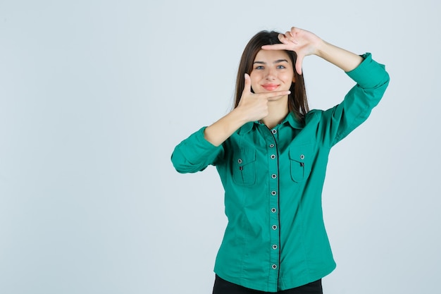 Belle jeune femme en chemise verte faisant le geste du cadre et à la joyeuse vue de face.