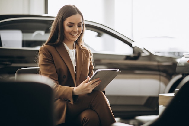 Belle jeune femme choisissant la voiture dans une salle d'exposition de voiture