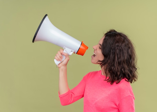 Photo gratuite belle jeune femme en colère parlant par haut-parleur debout en vue de profil sur mur vert isolé