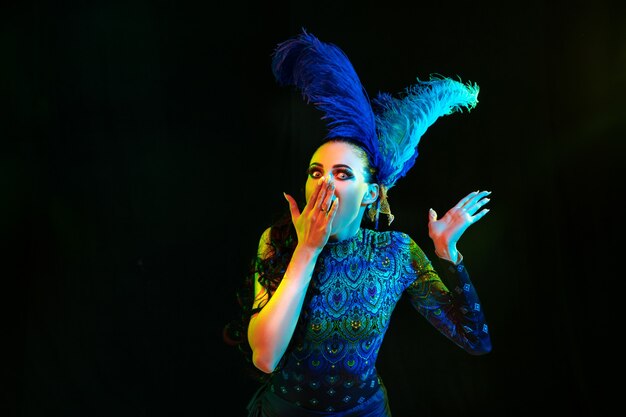 Belle jeune femme en costume de carnaval et de mascarade en néons colorés sur mur noir