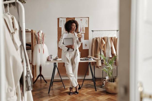 Belle jeune femme en costume élégant boit du café et tient un ordinateur portable