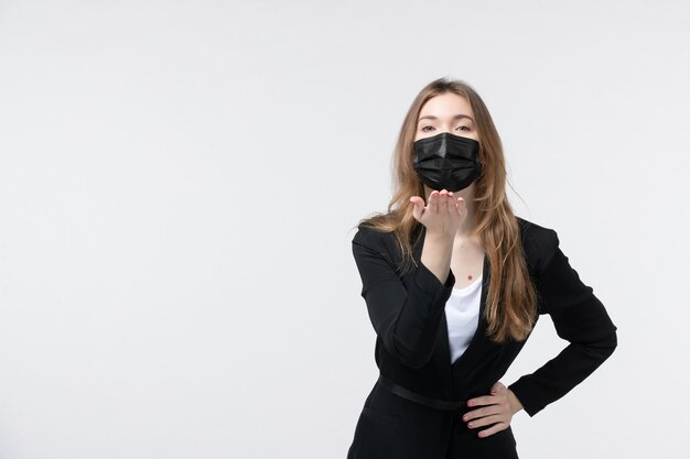 Belle jeune femme en costume portant un masque chirurgical et envoyant un geste de baiser sur blanc