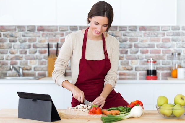 Belle jeune femme cuisine et à l&#39;aide de tablette numérique dans la cuisine.