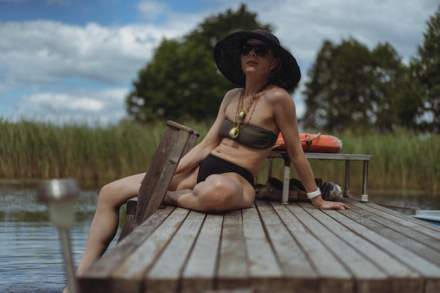 belle jeune femme dans un chapeau de paille noir se détend en été à l'extérieur au bord du lac, au bord de l'eau