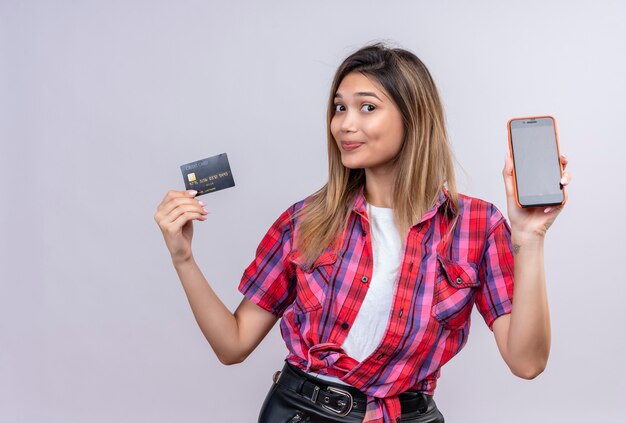 Une belle jeune femme dans une chemise à carreaux montrant l'espace vide du téléphone mobile et de la carte de crédit