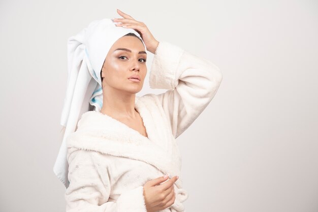 Photo gratuite belle jeune femme dans un peignoir blanc posant sur un mur blanc.