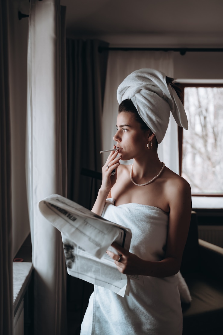 Photo gratuit belle jeune femme dans une serviette fume une cigarette et lit le journal