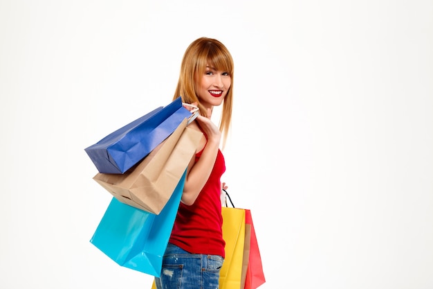 Belle jeune femme debout avec achats sur mur blanc