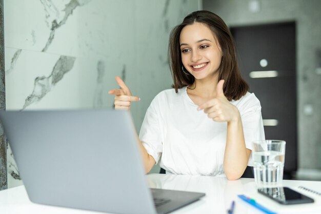 Belle jeune femme debout dans la cuisine à l'intérieur à la maison à l'aide de la cuisine d'ordinateur portable.