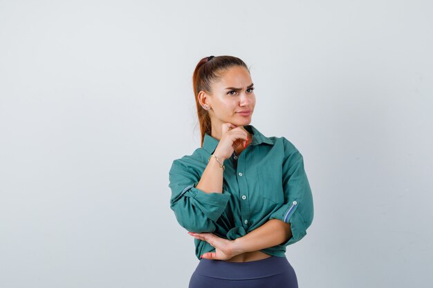 Belle jeune femme debout en pensant pose en chemise verte et à la perplexité. vue de face.