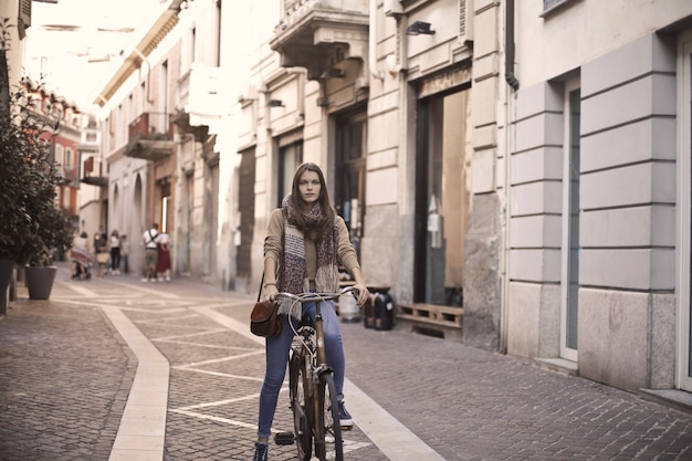 Belle jeune femme avec une écharpe et un jean faisant du vélo dans une rue confortable