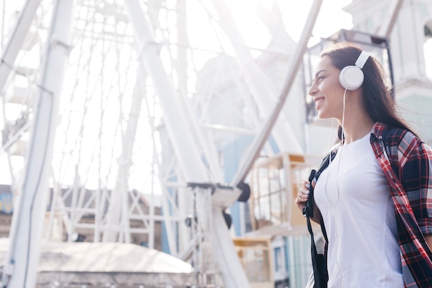 Belle jeune femme écoutant de la musique avec un casque, debout près de la grande roue