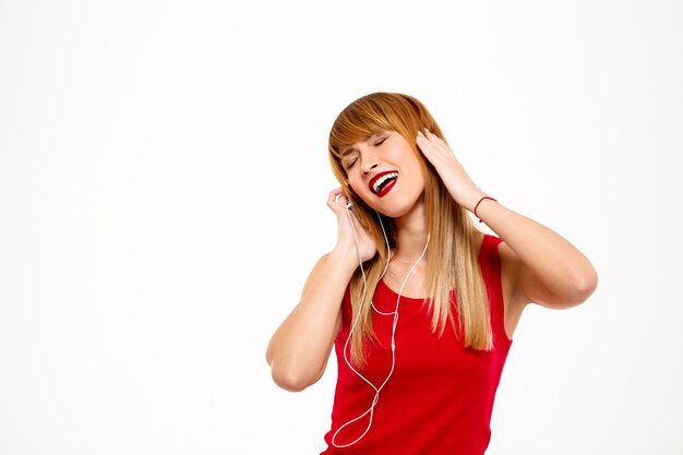 Belle jeune femme écoutant de la musique dans les écouteurs sur mur blanc