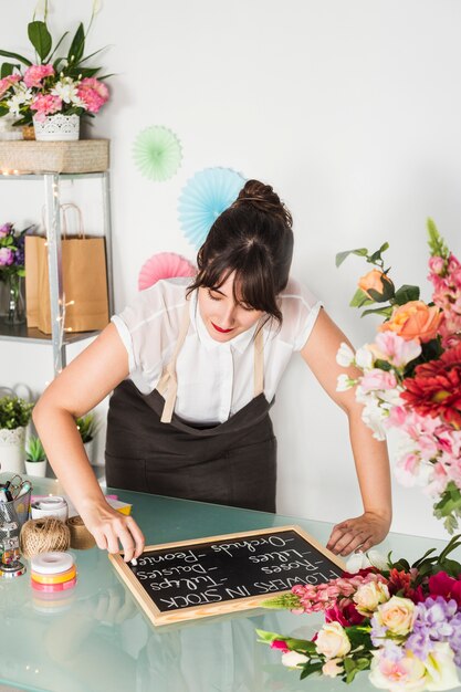 Belle jeune femme écrivant sur ardoise avec craie en magasin de fleurs