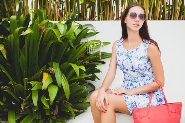 Belle jeune femme élégante en robe imprimée bleue, sac rouge, lunettes de soleil, tenue à la mode, vêtements à la mode, souriant, assis, été, accessoires