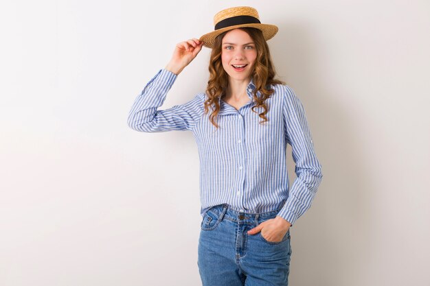 Belle jeune femme élégante en tenue de style été posant sur un mur blanc portant un chapeau de paille