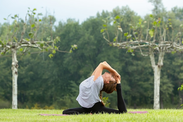 Belle jeune femme faisant des exercices d'yoga dans le parc verdoyant. Concept de mode de vie et de remise en forme sain.