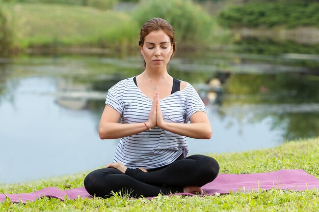 Belle jeune femme faisant des exercices d'yoga dans le parc verdoyant