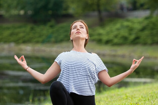 Belle jeune femme faisant des exercices d'yoga dans le parc verdoyant