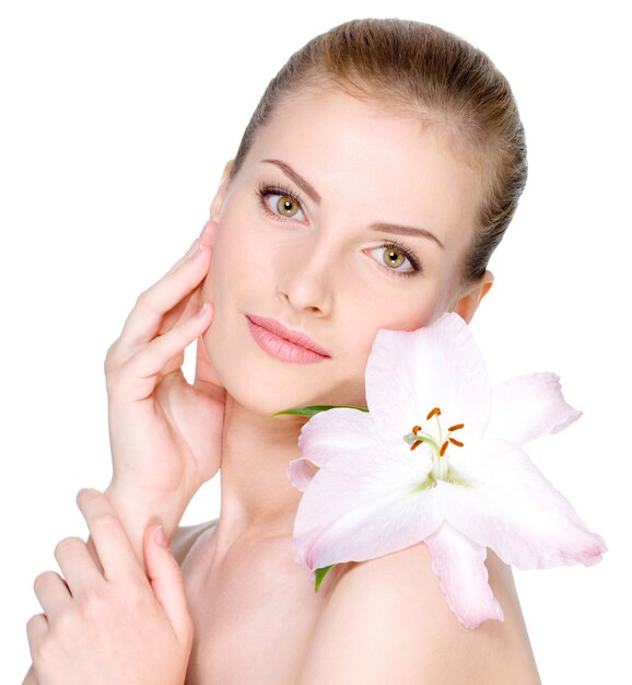 Belle jeune femme avec une fleur sur une épaule caressant son visage clair - isolé sur blanc