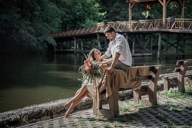 Une belle jeune femme avec des fleurs et son mari sont assis sur un banc et profitent de la communication, d'un rendez-vous dans la nature, de la romance dans le mariage.