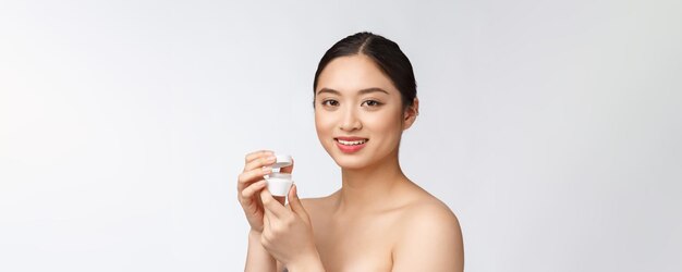 Belle jeune femme sur fond blanc isolé tenant une crème pour le visage cosmétique asiatique