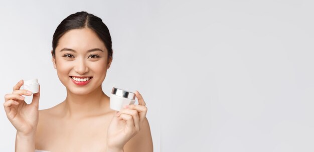 Belle jeune femme sur fond blanc isolé tenant une crème pour le visage cosmétique asiatique