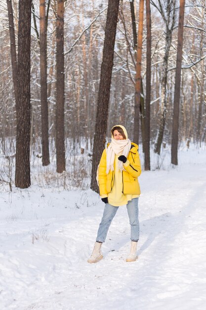 Belle jeune femme gaie dans une forêt d'hiver paysage enneigé s'amusant se réjouit en hiver et la neige dans des vêtements chauds