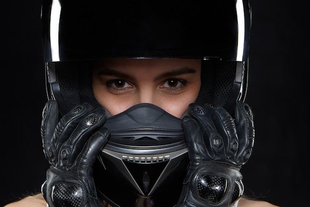 Belle jeune femme en gants de cuir noir et casque de moto de protection. Coureur de motocyclette féminin autodéterminé attrayant portant les mains et la protection du corps contre les chutes et les accidents