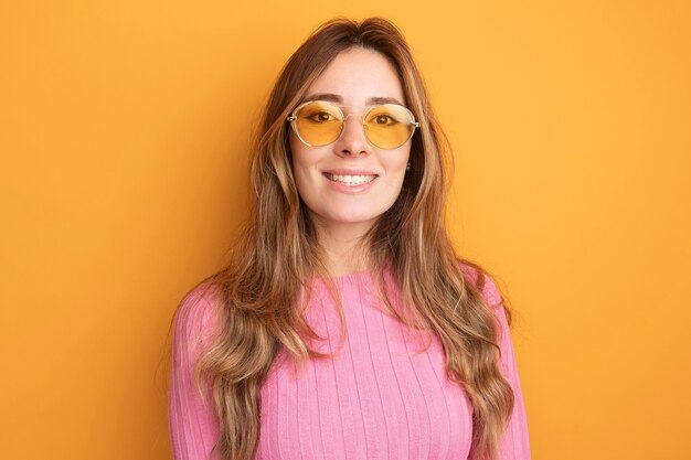 Belle jeune femme en haut rose portant des lunettes regardant la caméra souriant joyeusement