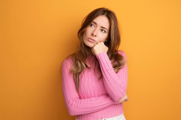 Belle jeune femme en haut rose regardant de côté avec une expression pensive pensant