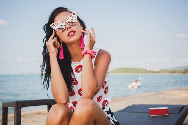 Belle jeune femme hipster sur la plage tropicale, lunettes de soleil, tenue élégante, vacances d'été, s'amuser, sourire, heureux, coloré, émotion positive, accessoires