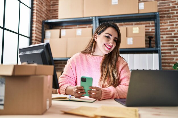 Belle jeune femme hispanique travaillant dans le commerce électronique à l'aide d'un smartphone au bureau