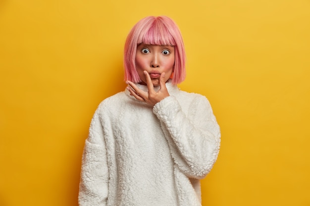 Photo gratuite une belle jeune femme impressionnée fait la moue et regarde avec des yeux écarquillés, fait la grimace, a les cheveux teints en rose, les joues rouges et une peau saine