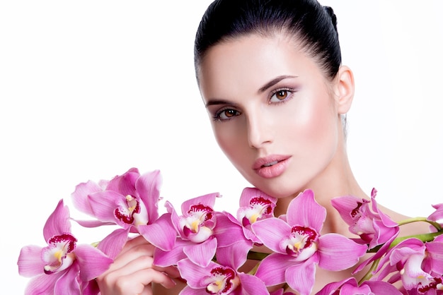 Photo gratuite belle jeune femme jolie avec une peau saine et des fleurs près du visage - isolé sur blanc.