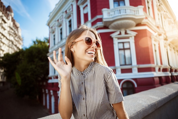 Belle jeune femme joyeuse à lunettes de soleil se promener dans la ville, souriant.