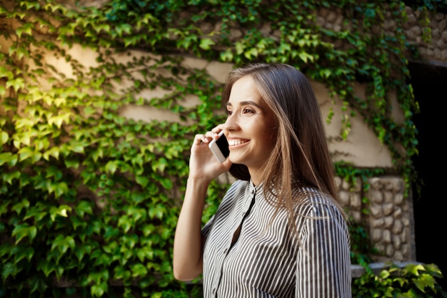 Belle jeune femme joyeuse se promener dans la ville, parlant au téléphone.