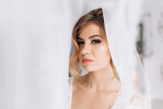 Belle jeune femme en lingerie blanche pose en peignoir de soie blanche dans une chambre d&#39;hôtel lumineuse