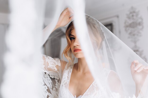 Belle jeune femme en lingerie blanche pose en peignoir de soie blanche dans une chambre d&#39;hôtel lumineuse