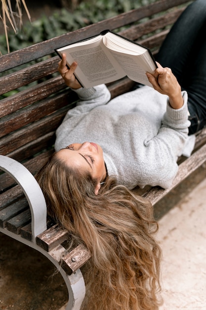 Belle jeune femme lisant un livre sur un banc