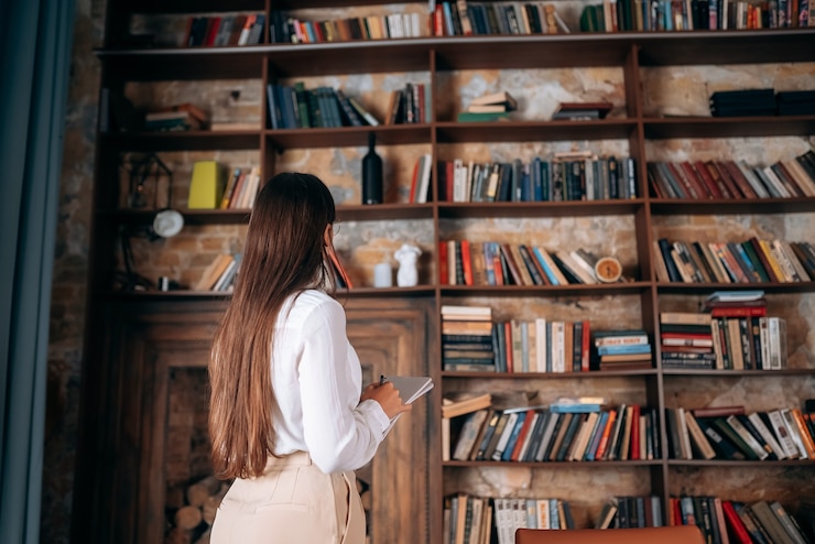 Photo gratuit belle jeune femme avec des lunettes tenant un cahier et regardant la bibliothèque