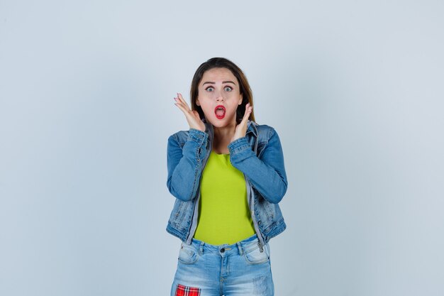 Belle jeune femme avec les mains près du visage en tenue de denim et l'air effrayé. vue de face.