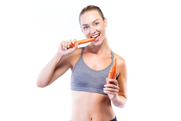 Belle jeune femme mangeant des carottes sur fond blanc.