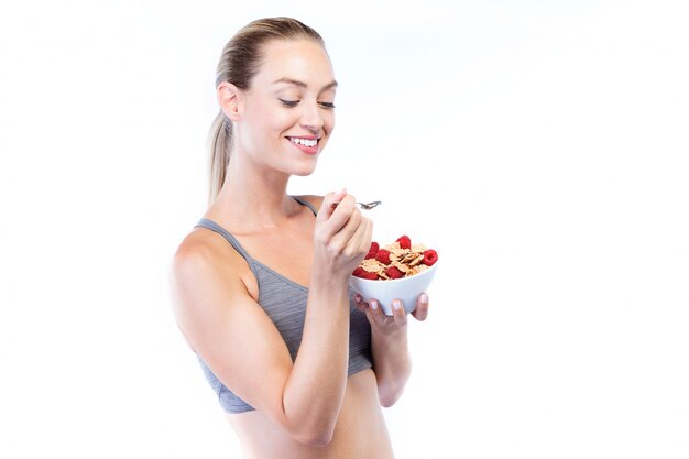 Belle jeune femme mangeant des céréales et des fruits sur fond blanc.