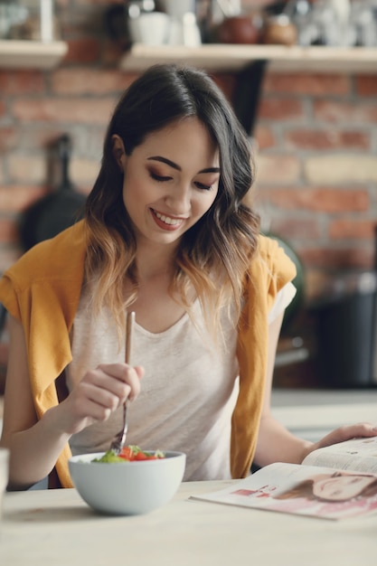 Belle jeune femme mangeant une salade saine et lisant un magazine