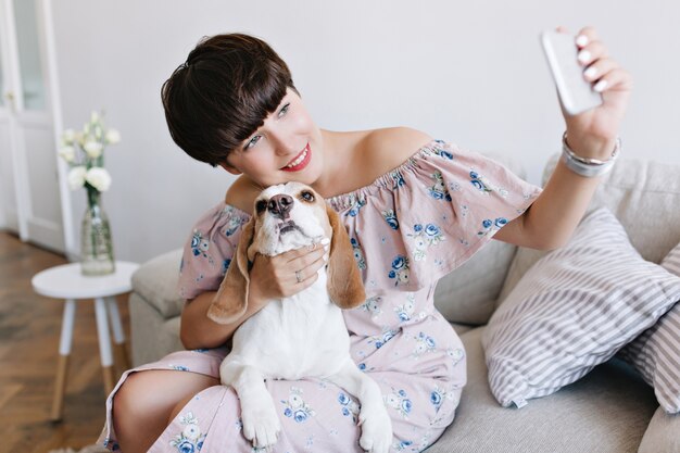 Belle jeune femme avec un maquillage nude touchant avec amour son chien beagle et prenant une photo d'elle-même