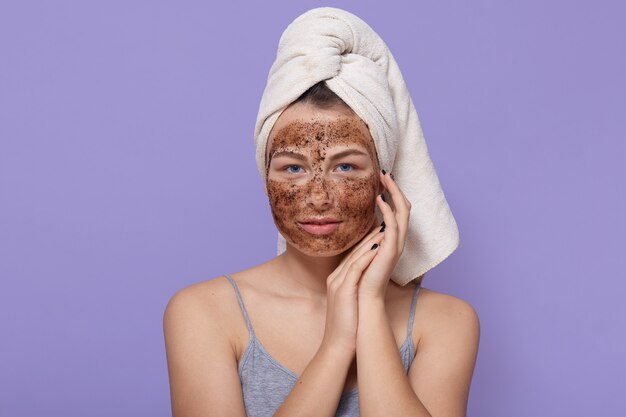 Belle jeune femme avec masque au chocolat sur le visage, pose avec une serviette blanche sur la tête