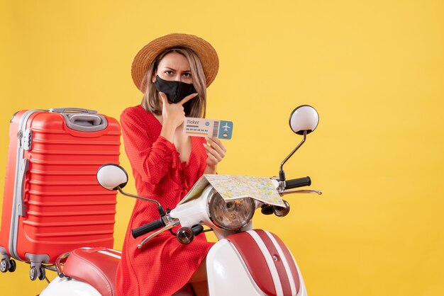 belle jeune femme avec masque noir sur cyclomoteur holding ticket